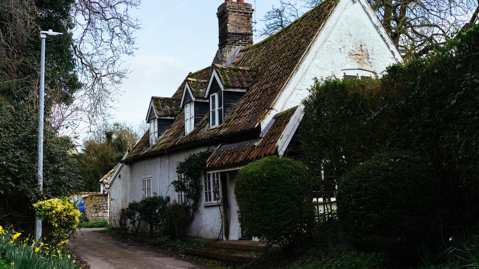 Altes Landhaus mit Gauben und Garten an einem schmalen Weg