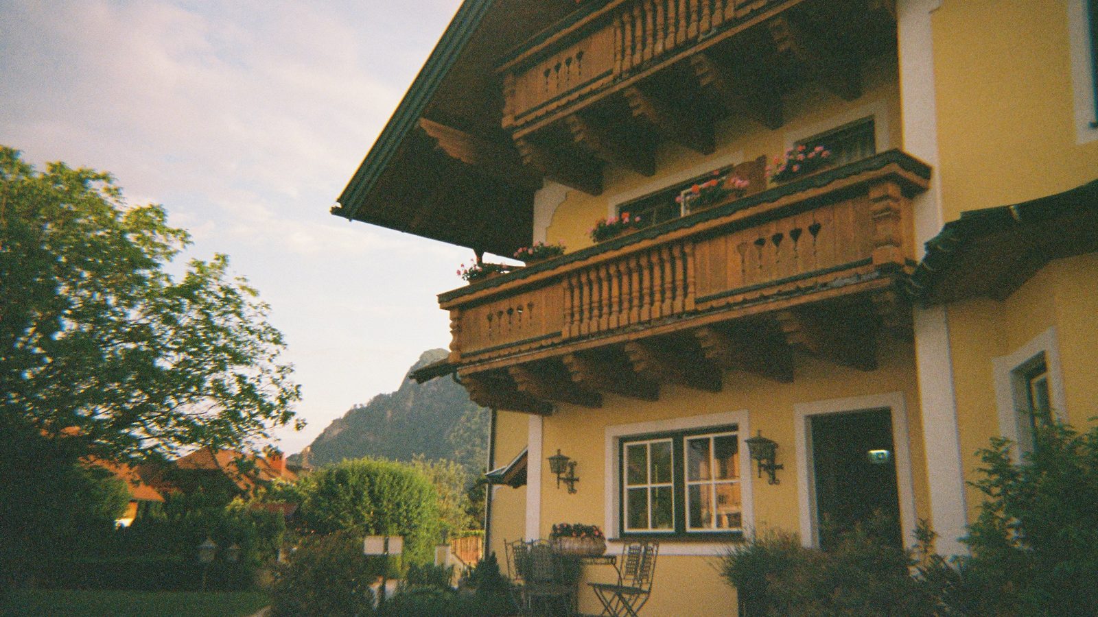 Gelbes Haus mit Holzbalkonen und Terrasse vor Bergkulisse